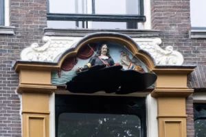 Bijzonder aan het historische pand Oudezijds Voorburgwal 136 is de gevelsteen. Dit is een houtsnijwerk van admiraal Cornelis Tromp, een beroemde zeevaarder (1629 tot 1690). Het hout was behoorlijk verwaarloosd, maar is na een jaar onderhoud volledig in ere hersteld en teruggeplaatst boven de deur. Alleen wel met een belangrijke aanvulling. Namelijk een zwarte vlek bij het houtsnijwerk. Deze staat symbool voor de historische periode waarin niet enkel overwinningen maar ook onderdrukking, slavernij en armoede onderdeel waren van het bestaan. Deze gevelsteen schetst een completer beeld van die periode.